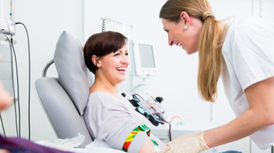 Smiling middle-aged woman donating blood at a New York Blood Center with smiling phlebotomist attending to her.
